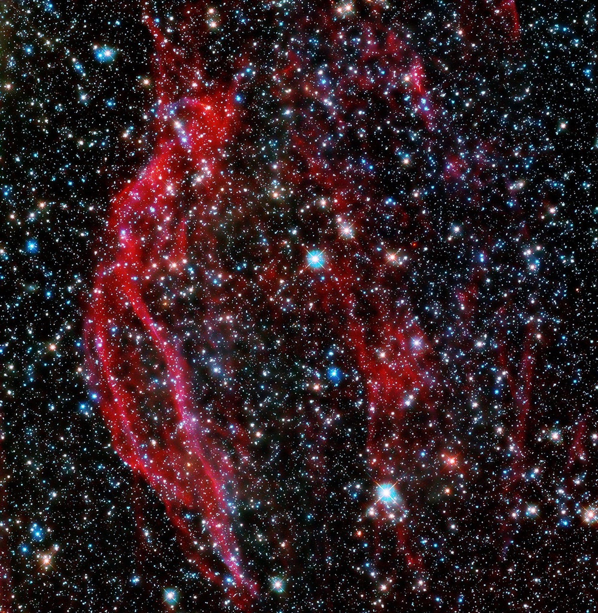 A field full of stars of all different colors, with several deep red tendrils/streaks of gas running from top to bottom near the center.